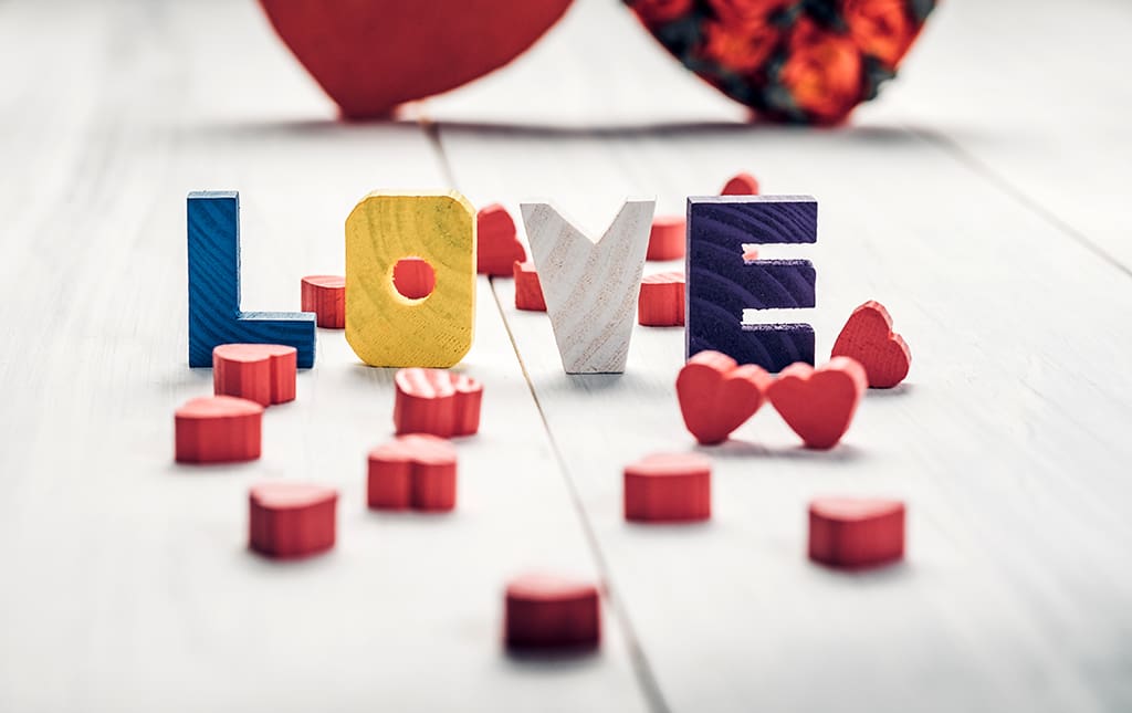 Wooden blocks spelling out the word "love" and wooden hearts on a white vintage tabletop