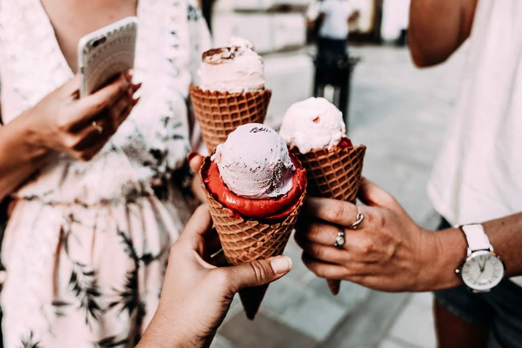 3 people with double-scooped ice cream cones cheersing the cones