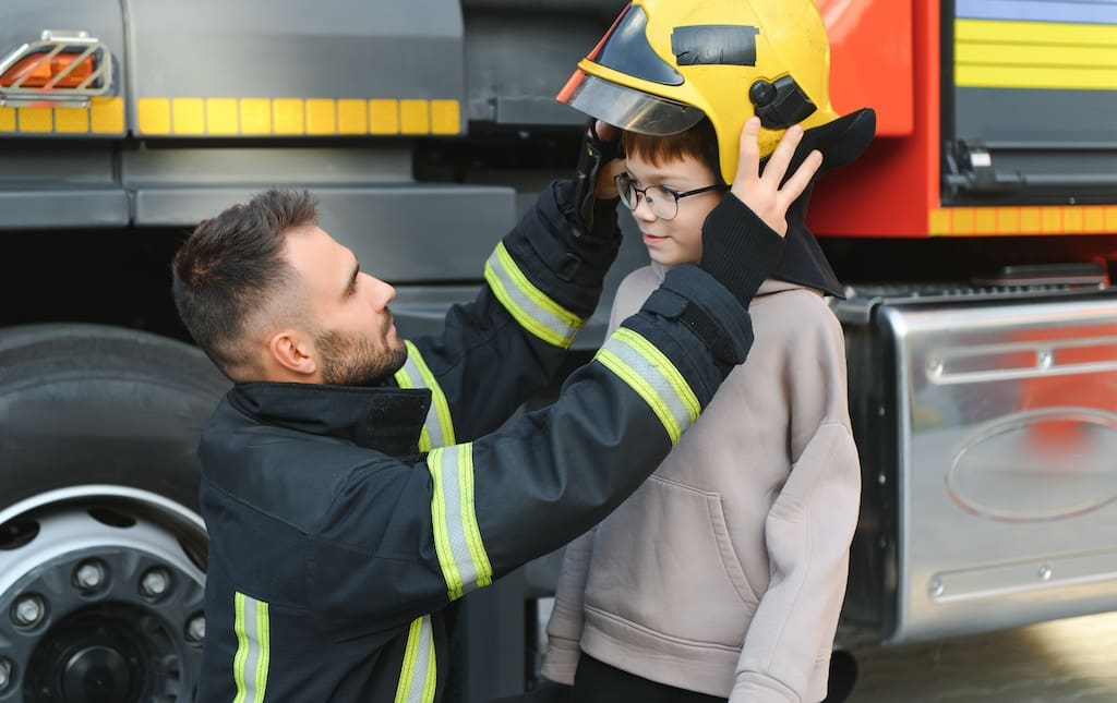 Firefighter trying a firefighting helmet on a young boy during his tour of the fire department