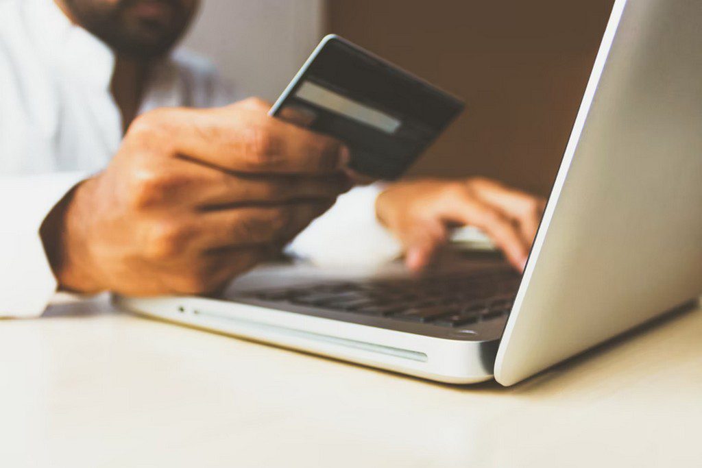 A man holding his credit card in front of a laptop