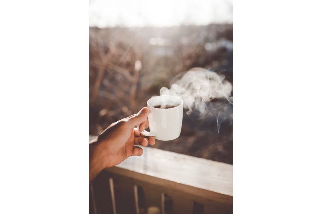 A hand holding a coffee mug on a balcony