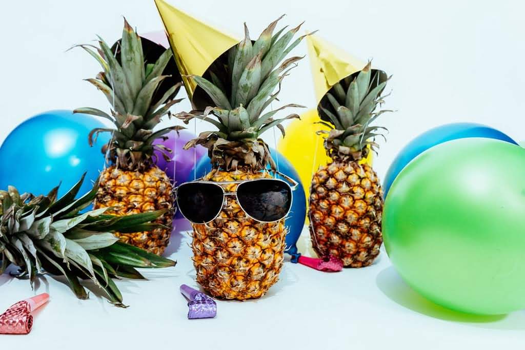 A pineapple with sunglasses surrounded by colorful balloons