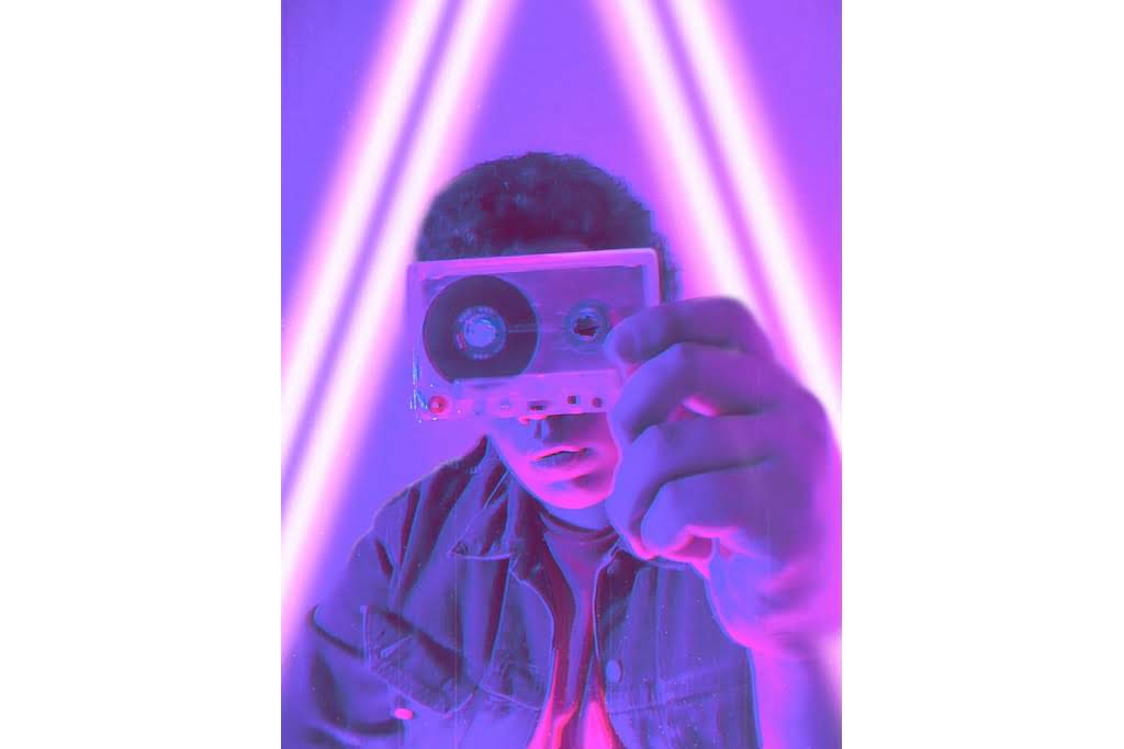 A man under purple light who is looking at a cassette tape