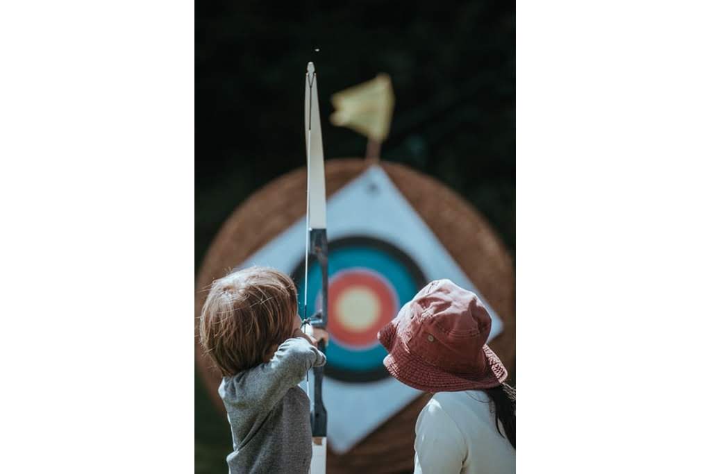 A little boy shooting a bow while a girl watches