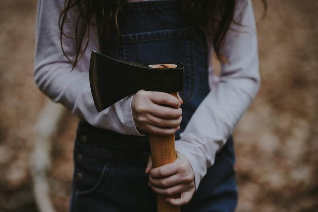 A person in overalls and long hair holding an axe