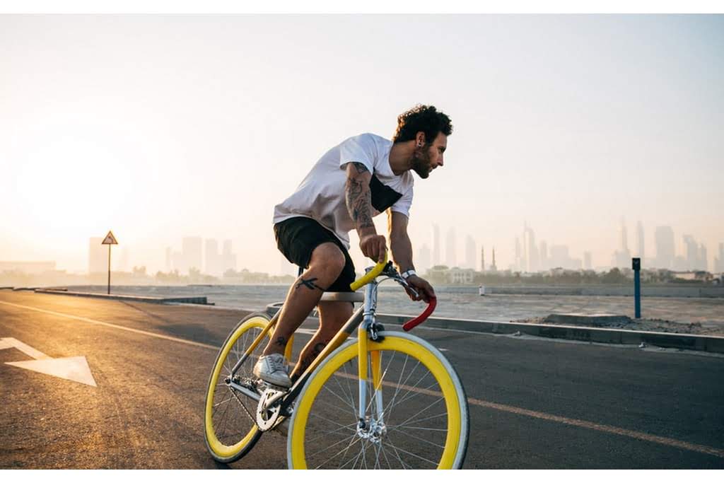 A man rides a bicycle with yellow wheels on a road