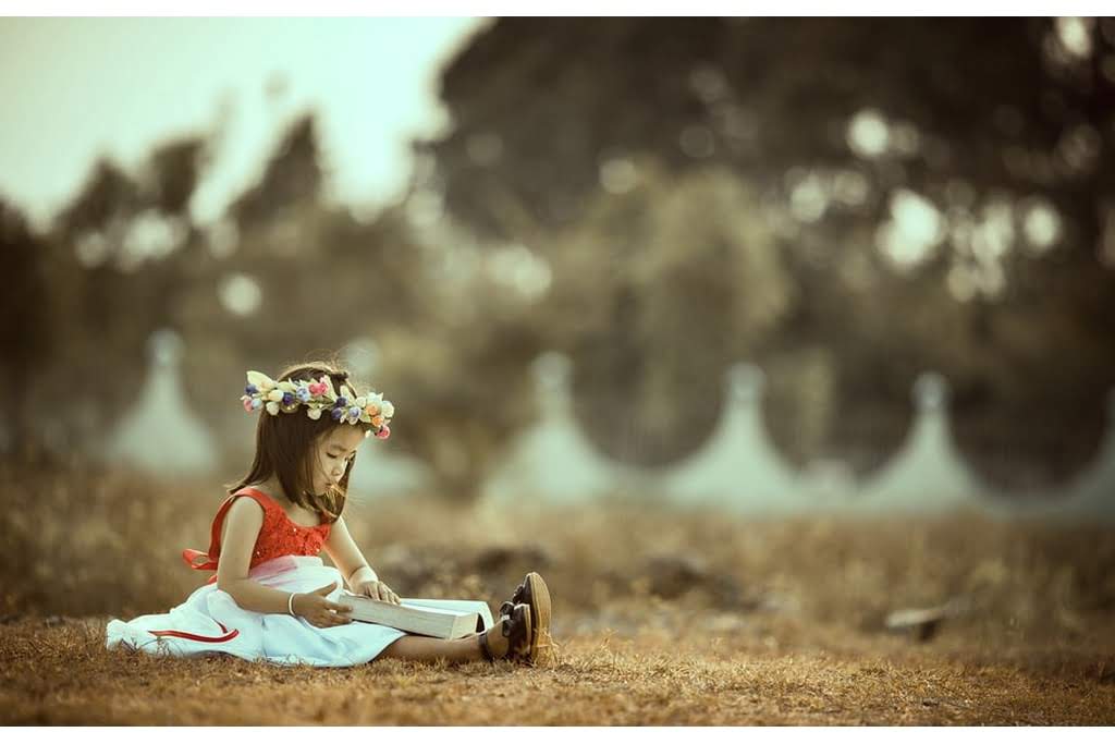 A little girl reading a book in a field with a flower crown