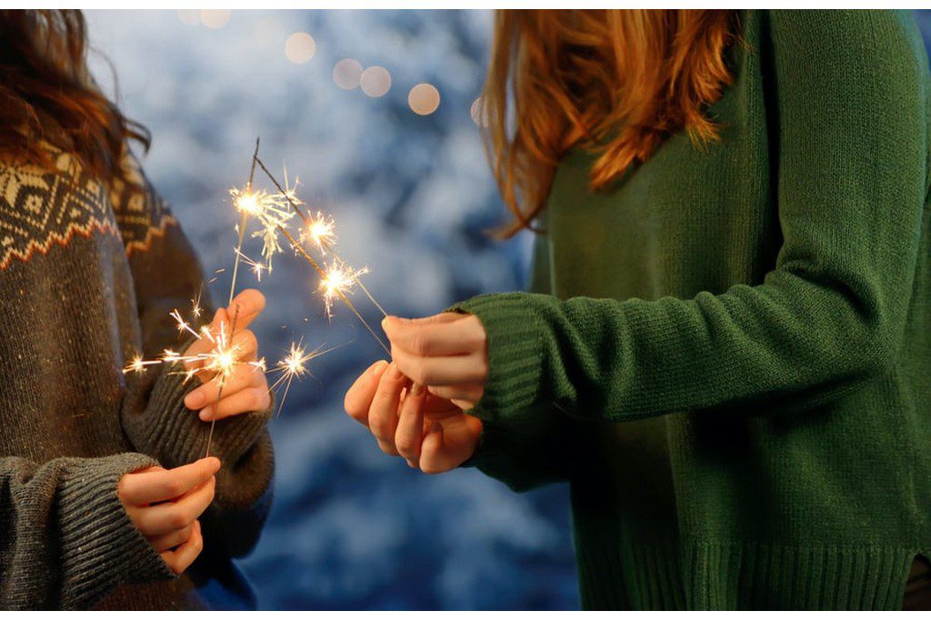 Two women in green sweatshirts holding sparklers