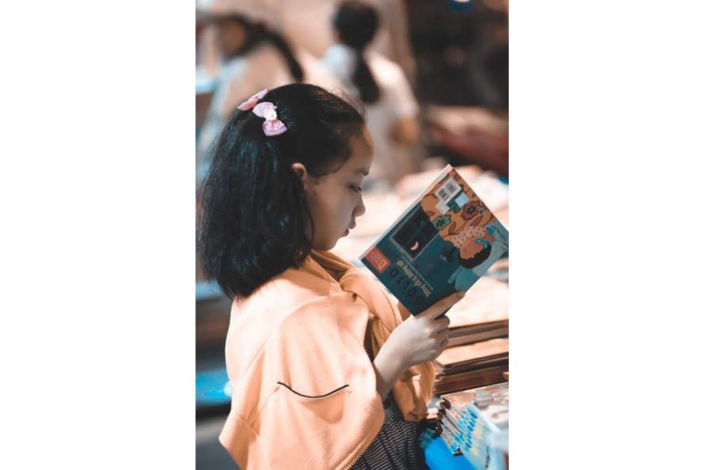 A little girl reading a book at a table