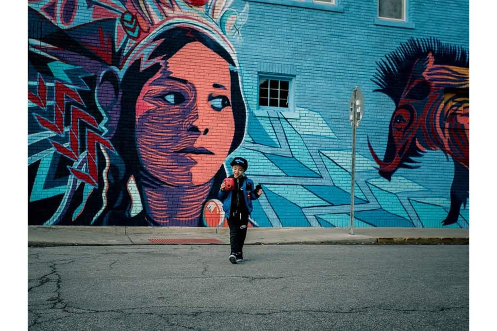 A child looking at a red camera in front of a mural