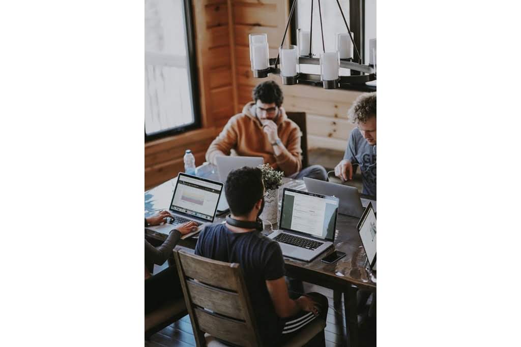 4 men sitting around a table and looking at their computers