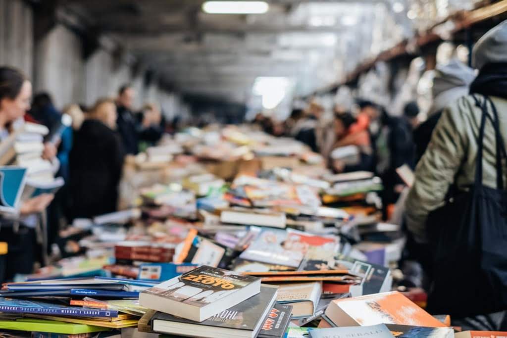 A table covered in books with people browsing book sale fundraiser