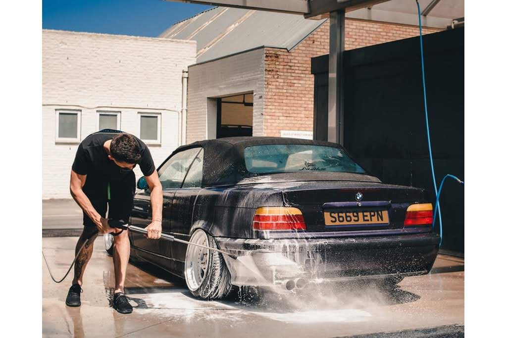 A White man washes an older car with a hose car wash