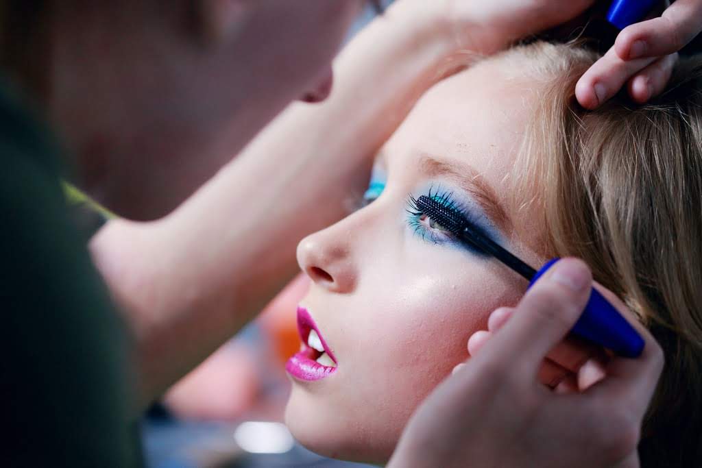 A woman puts eye makeup on a Caucasian girl mom putting makeup on kid