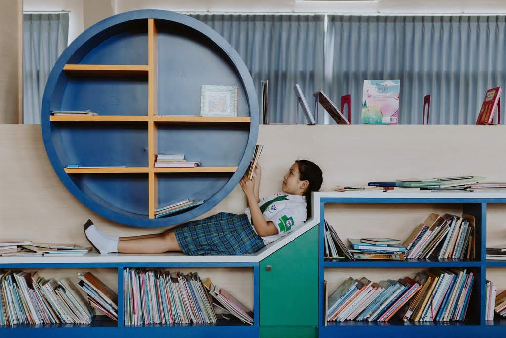 An Asian girl sitting on a bookshelf gilf laying on bookcase