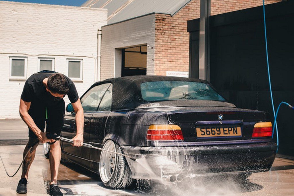A White teen boy washes a car with a hose kid doing a car wash