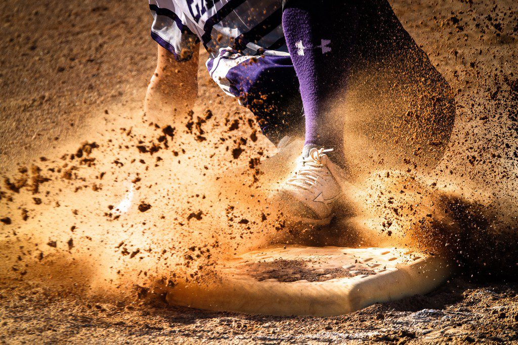 A person slides through on a base in baseball with dirt flying everywhere sliding on base in baseball