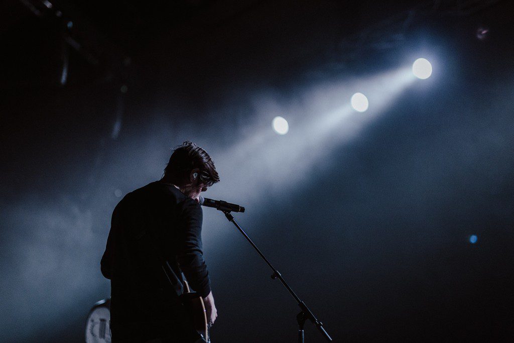 A white man plays an instrument under a spotlight performance at the concert
