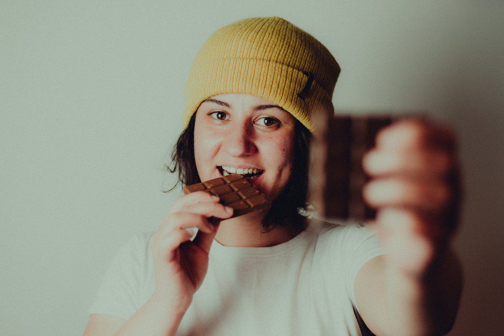 A White woman eats a bar of chocolate while smiling kid eating chocolate