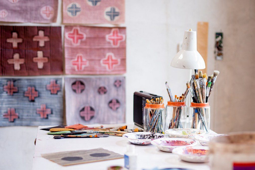 A white table is covered with paintbrushes and paintings art supplies