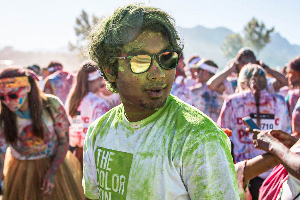 An Asian man in sunglasses, covered in green powder in a crowd color run participants