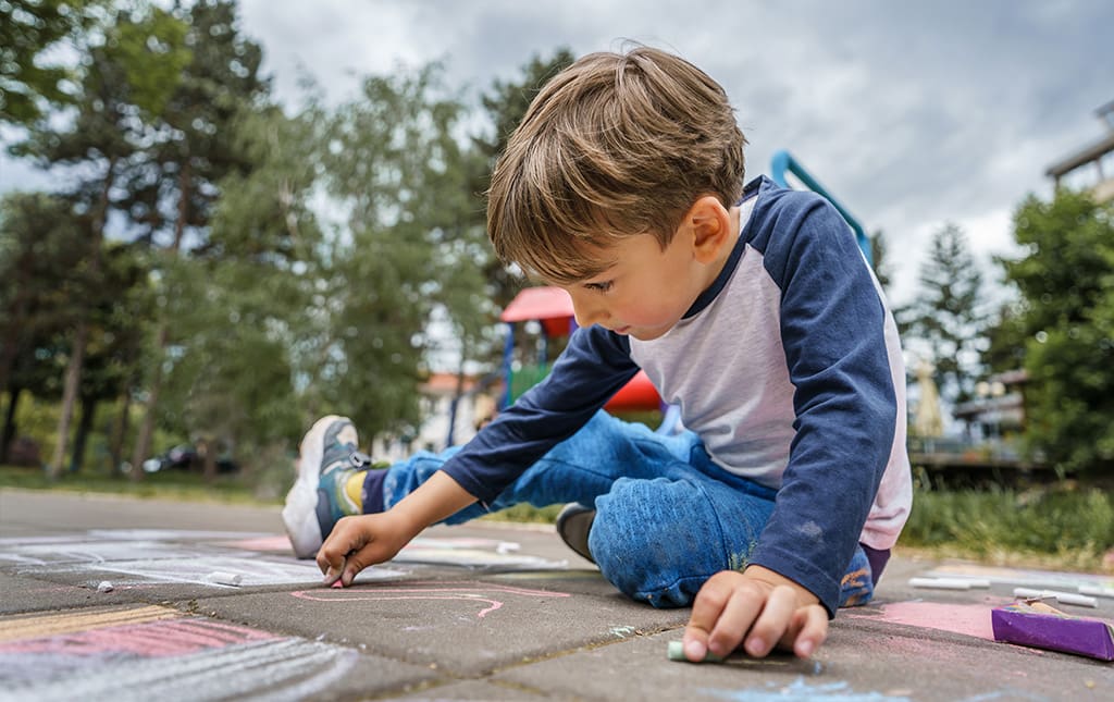 Young child in pre school drawing on pavement with chalk