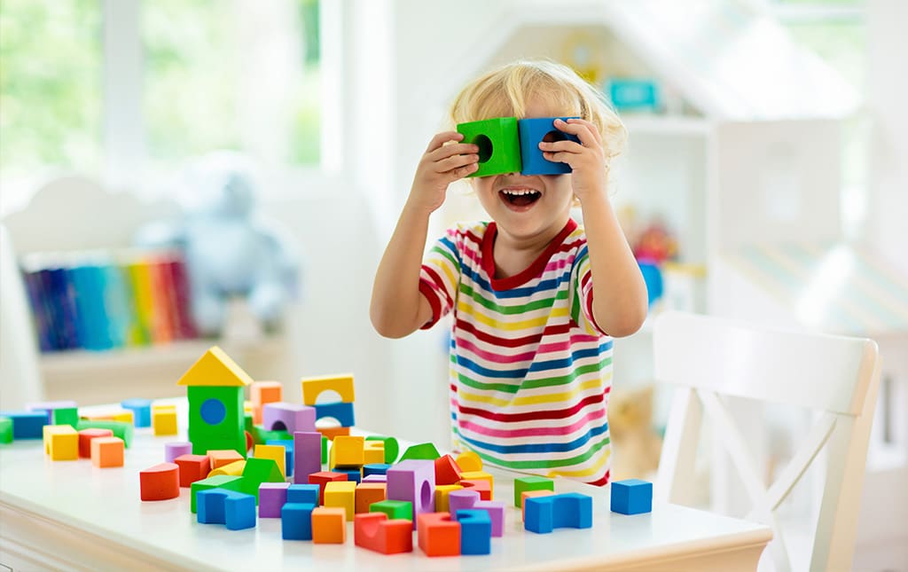 Young pre-school student playing with colorful block toys while smiling 