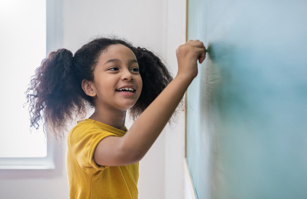 Girl writing on word wall on classroom blackboard