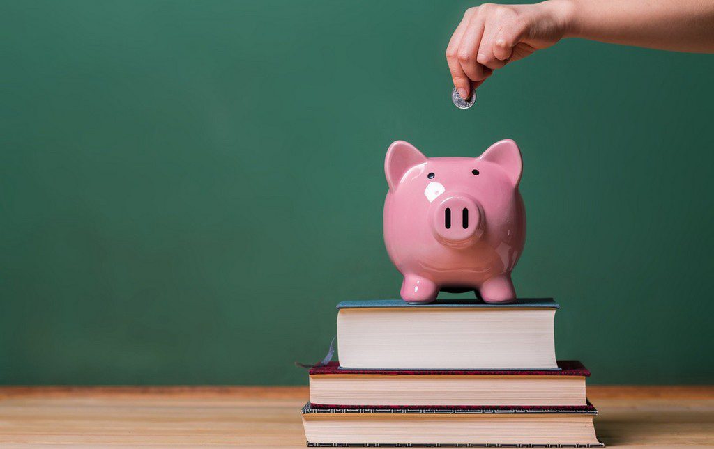 Hand dropping money into piggy bank on top of book stack to represent fundraising for classroom library