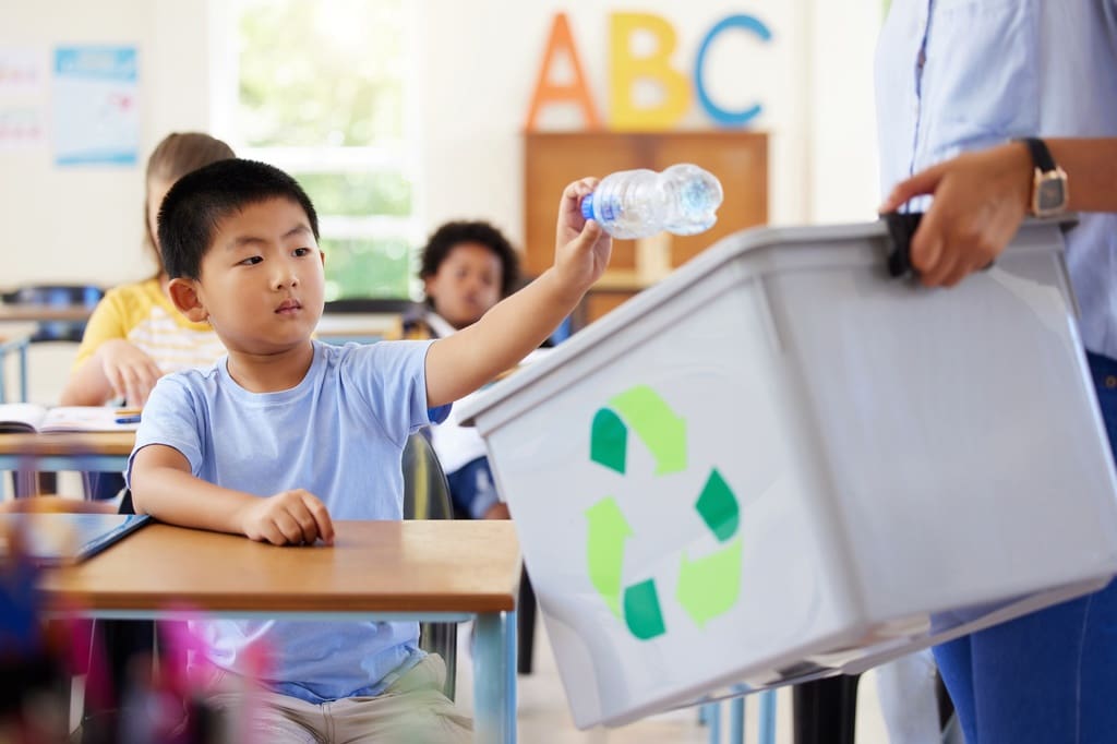 Elementary student adding bottle to bin during eco-friendly recycling drive fundraiser