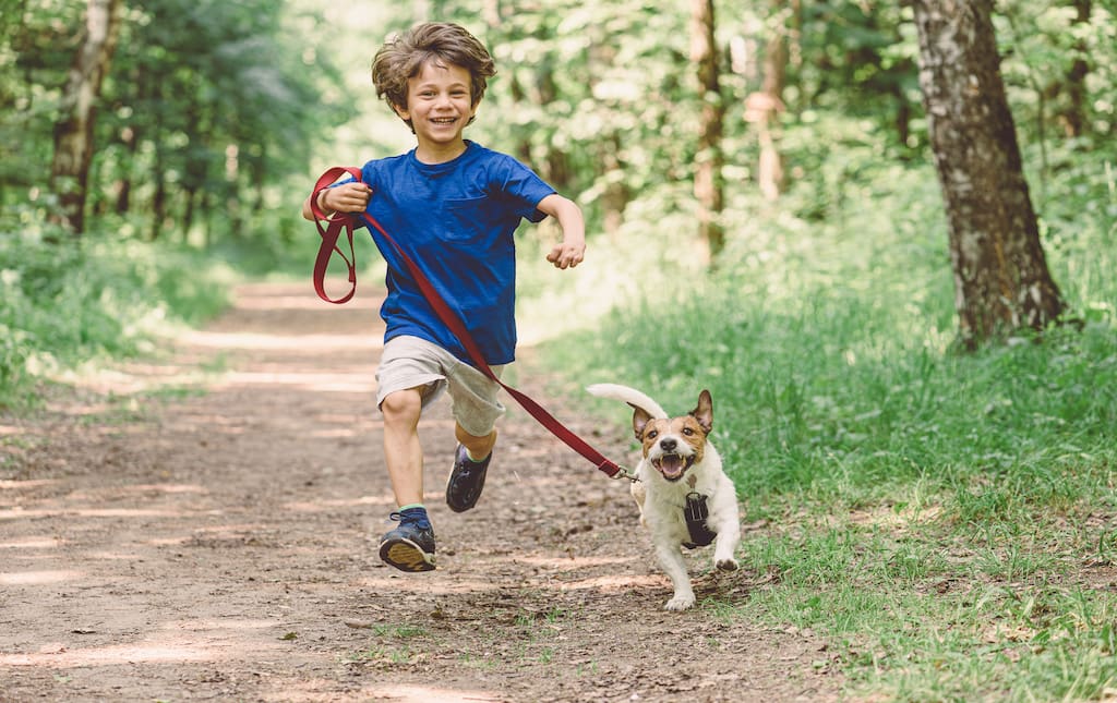 young boy running with a dog on a leash outside