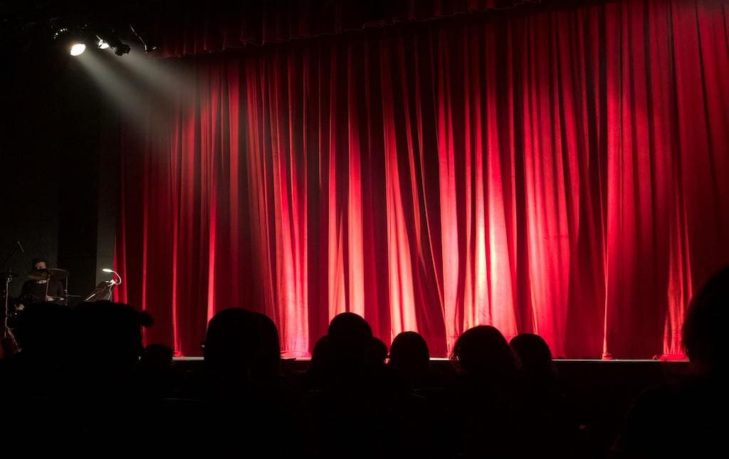 people in a theatre waiting for the red curtain to open